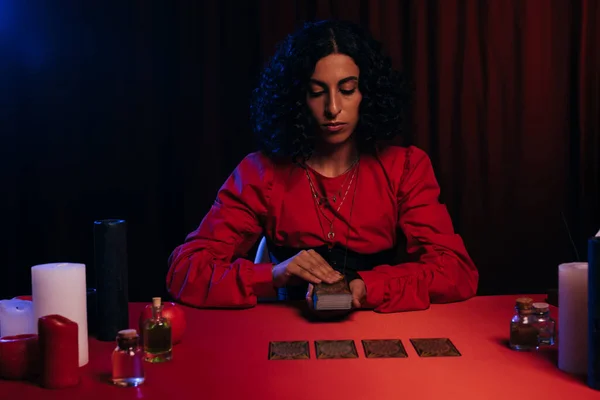 KYIV, UKRAINE - JUNE 29, 2022: young woman predicting future on tarot cards on red table and dark background — Stock Photo