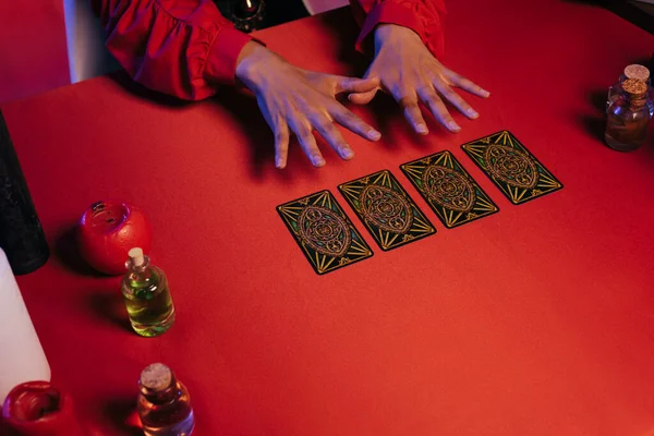 KYIV, UKRAINE - JUNE 29, 2022: partial view of medium predicting future with tarot cards near essential oils on red table — Stock Photo