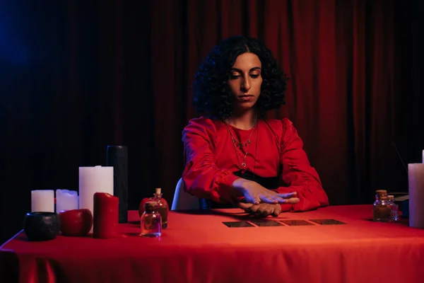 Medium holding hand over tarot cards near candles and essential oils on dark background — Fotografia de Stock