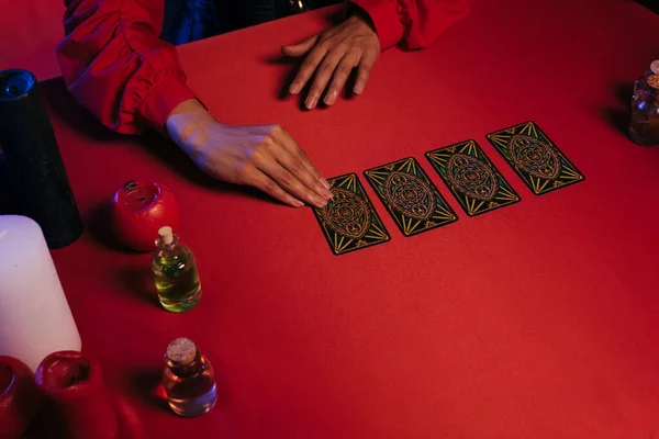 KYIV, UKRAINE - JUNE 29, 2022: partial view of fortune teller divinating on tarot cards on red table near essential oils and candles — Stockfoto