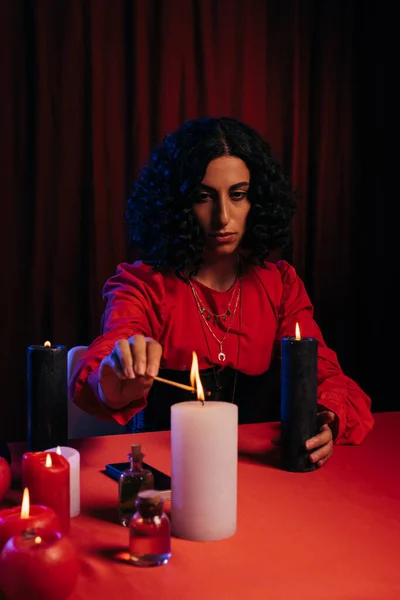 Brunette fortune teller lighting palo santo stick during meditation session on dark background — Photo de stock