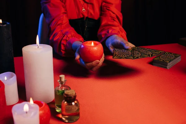 KYIV, UKRAINE - JUNE 29, 2022: cropped view of oracle with tarot cards and burning candle isolated on black — Stock Photo