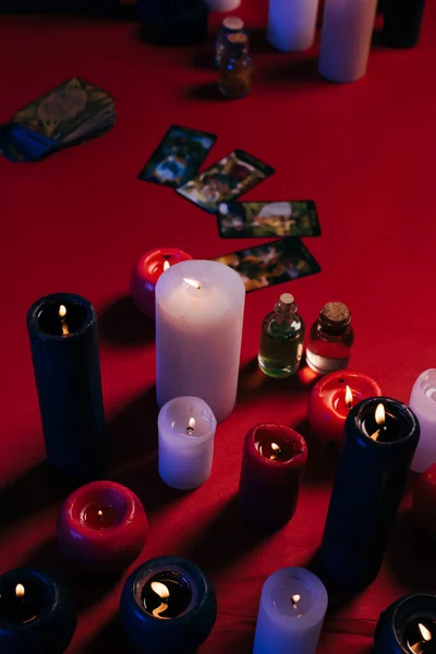 KYIV, UKRAINE - JUNE 29, 2022: high angle view of burning candles and tarot cards on red table — стоковое фото