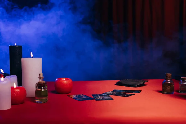 KYIV, UKRAINE - JUNE 29, 2022: burning candles and tarot cards on red table near blue smoke on black background — Stock Photo