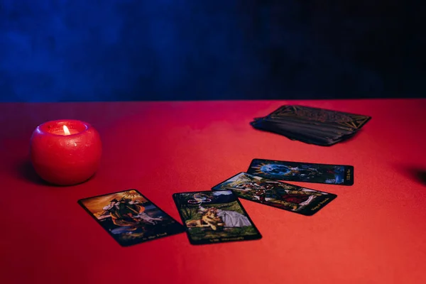 KYIV, UKRAINE - JUNE 29, 2022: tarot cards and burning candle on red table and black background with blue smoke — Fotografia de Stock