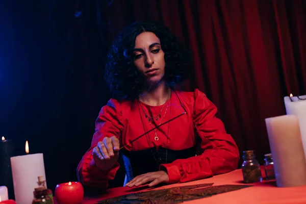 Young fortune teller holding palo santo stick near tarot cards on dark background - foto de stock