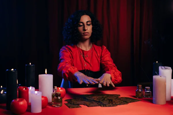 KYIV, UKRAINE - JUNE 29, 2022: fortune teller divinating on tarot cards near burning candles on red table in darkness — Stock Photo