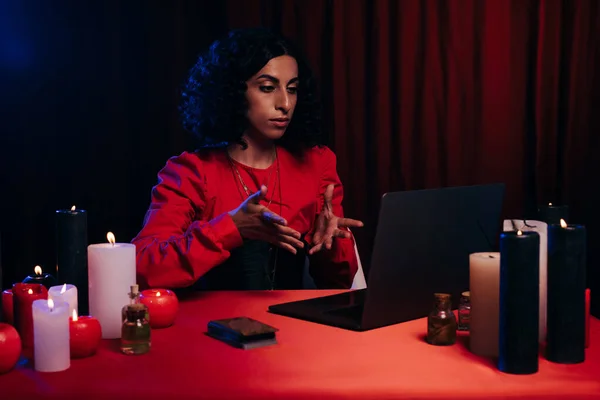 Brunette future teller pointing at laptop during online spiritual session on dark background — Fotografia de Stock