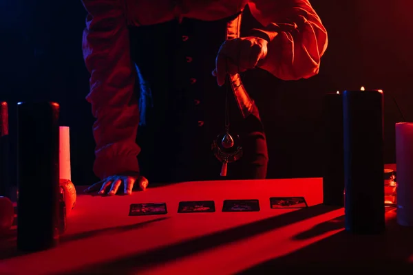 Partial view of oracle with amulet over tarot cards on red table isolated on black — Stock Photo