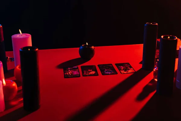 KYIV, UKRAINE - JUNE 29, 2022: tarot cards and burning candles on red table isolated on black — Stockfoto