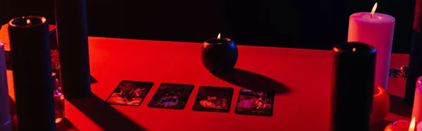 KYIV, UKRAINE - JUNE 29, 2022: red table with candles and tarot cards isolated on black, banner — Photo de stock