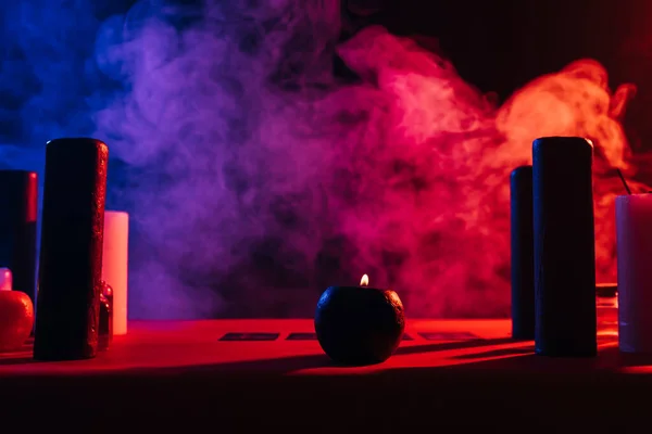Candles and tarot cards near colorful smoke on black background — Photo de stock