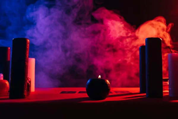 Candles and tarot cards near colorful smoke on black background — Stock Photo