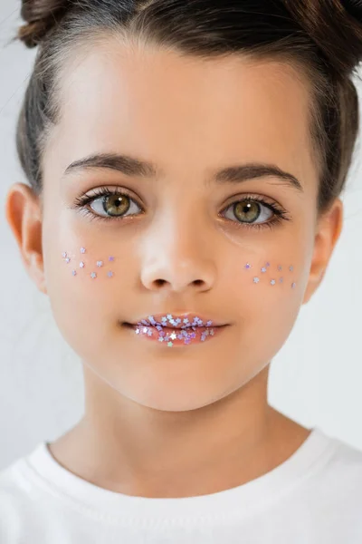 Portrait of adorable girl with sparkling glitter stars on face and lips looking at camera isolated on grey — Stockfoto