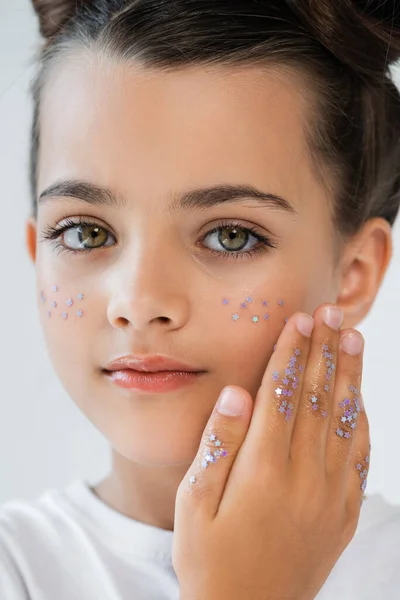 Close up of adorable girl with sparkling glitter stars on face looking at camera isolated on grey - foto de stock