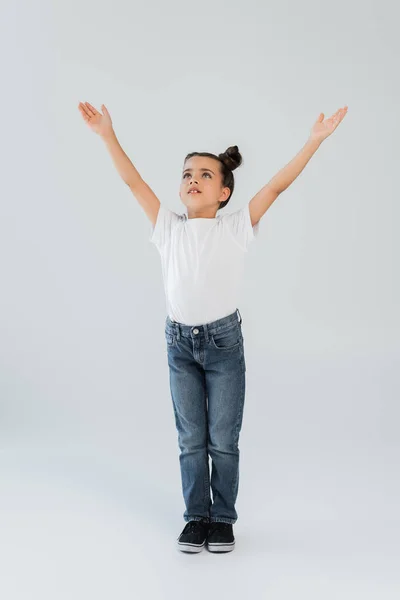 Full length of adorable girl with sparkling glitter stars on cheeks standing with outstretched hands on grey — Stock Photo