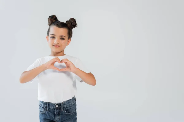 Cheerful girl with sparkling glitter stars on cheeks showing heart with hands isolated on grey — Stockfoto