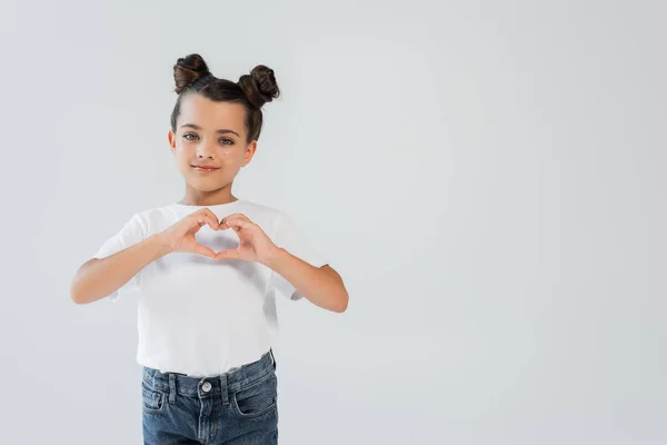 Cheerful girl with sparkling glitter stars on cheeks showing heart with hands isolated on grey — Fotografia de Stock