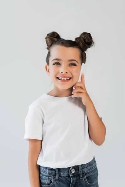 Joyful girl with glitter stars on cheeks talking on smartphone isolated on grey — Stock Photo