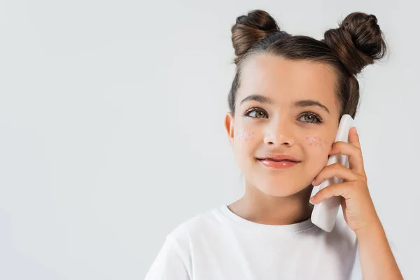 Усміхнена дівчина з блискучими зірками на щоках розмовляє на мобільному телефоні ізольовано на сірому — стокове фото