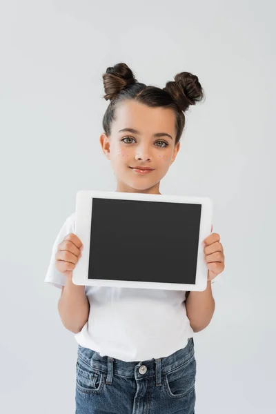 Adorable girl with glitter stars on cheeks smiling while holding digital tablet with blank screen isolated on grey — Photo de stock