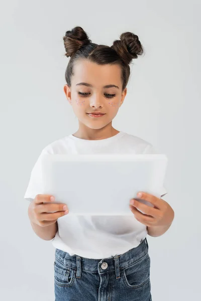 Cute girl with glitter stars on cheeks using digital tablet isolated on grey — Fotografia de Stock