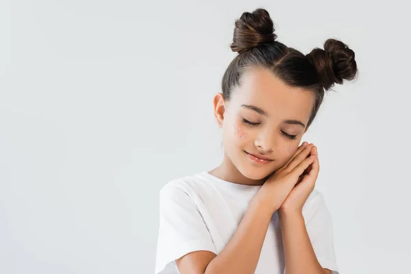 Sleepy girl with folded hands and glitter stars on cheeks posing isolated on grey — Photo de stock