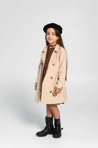 Full length of adorable girl in stylish trench coat and beret posing on grey — Photo de stock