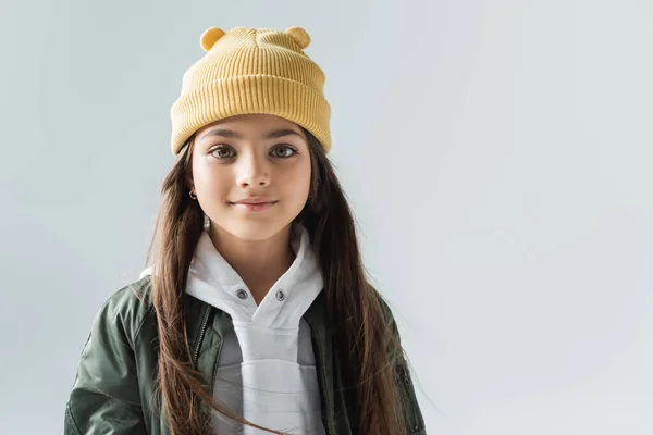 Portrait of cheerful kid in yellow beanie hat and bomber jacket looking at camera isolated on grey — Fotografia de Stock