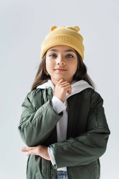 Cheerful girl in yellow beanie hat and bomber jacket looking at camera isolated on grey — Photo de stock