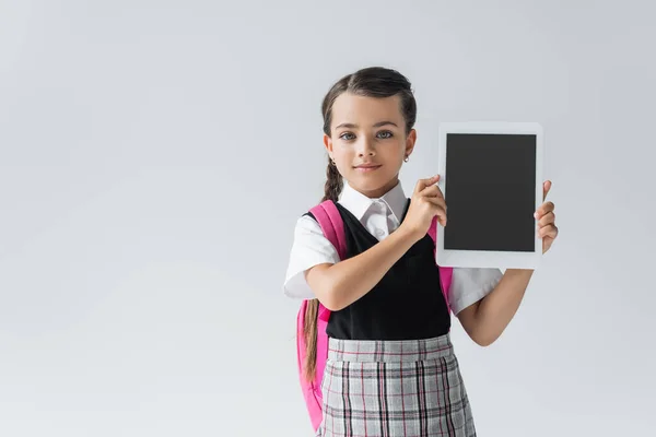 Cute schoolgirl in uniform holding digital tablet with blank screen and smiling isolated on grey — Photo de stock