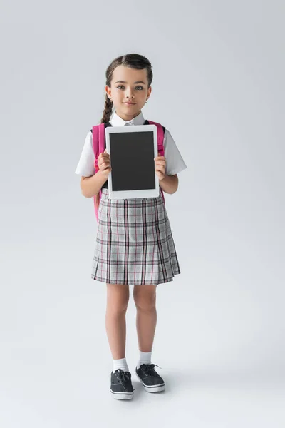 Full length of cute schoolgirl in uniform holding digital tablet with blank screen on grey — Stock Photo