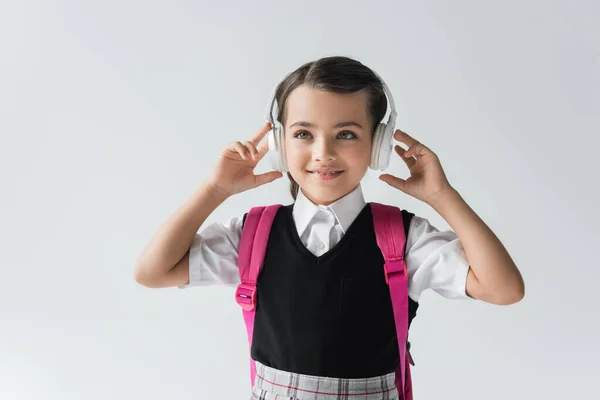 Cheerful schoolgirl in wireless headphones listening music isolated on grey — Stock Photo