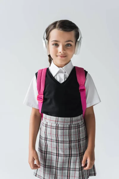 Щаслива школярка в бездротових навушниках слухає музику ізольовано на сірому — стокове фото