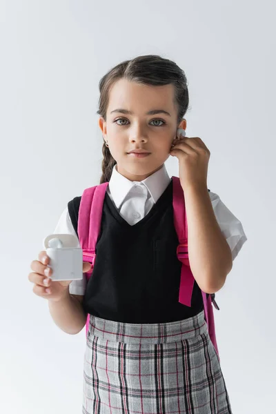 Cute schoolgirl holding earphone case and listening music isolated on grey — Stockfoto