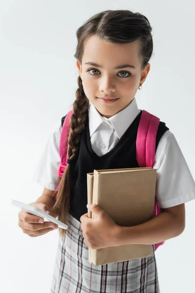 High angle view of smiling schoolgirl holding smartphone and books isolated on grey — Photo de stock