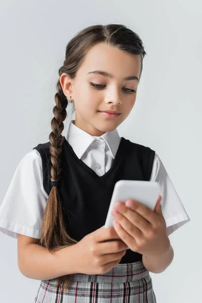 Cute girl in school uniform using smartphone isolated on grey — Stockfoto