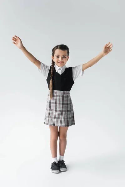 Full length of excited schoolkid in uniform standing with outstretched hands on grey — Stockfoto