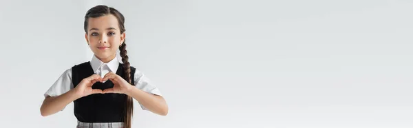 Portrait of happy schoolgirl showing heart with hands isolated on grey, banner — Fotografia de Stock