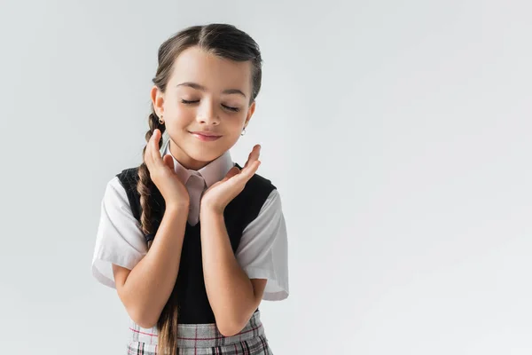 Portrait of happy schoolgirl with closed eyes gesturing isolated on grey — стоковое фото