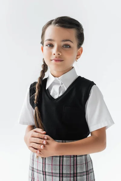 Portrait of schoolgirl with white shirt and vest looking at camera isolated on grey — стоковое фото