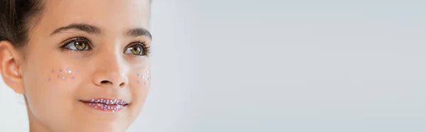 Portrait of cheerful girl with sparkling glitter stars on lips and face looking away isolated on white, banner — Stockfoto