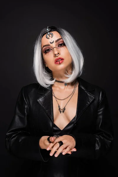 Verführerische Frau in Halloween-Make-up und Lederjacke, die isoliert auf schwarz in die Kamera blickt — Stockfoto