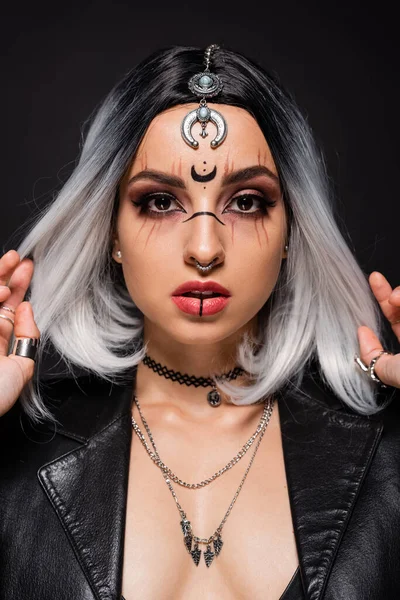 Portrait of woman in witch makeup and accessories touching ash blonde hair isolated on black — Stock Photo