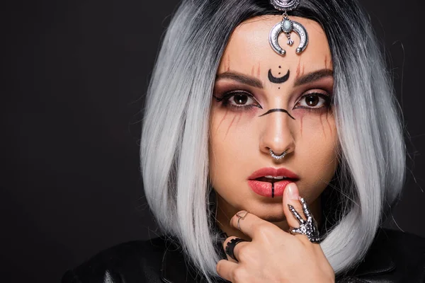Porträt einer Frau mit Hexenhalloween-Make-up, die Lippe berührt und isoliert auf schwarz in die Kamera schaut — Stockfoto