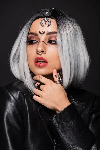 Verführerische Frau mit Hexen-Halloween-Make-up, die ihr Kinn berührt und isoliert auf schwarz wegschaut — Stockfoto