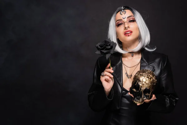 Sexy witch style woman with golden skull and dark rose on black background — Stock Photo