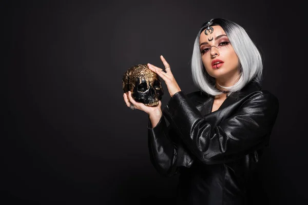 Woman in witch halloween costume and makeup posing with golden skull isolated on black — Stock Photo