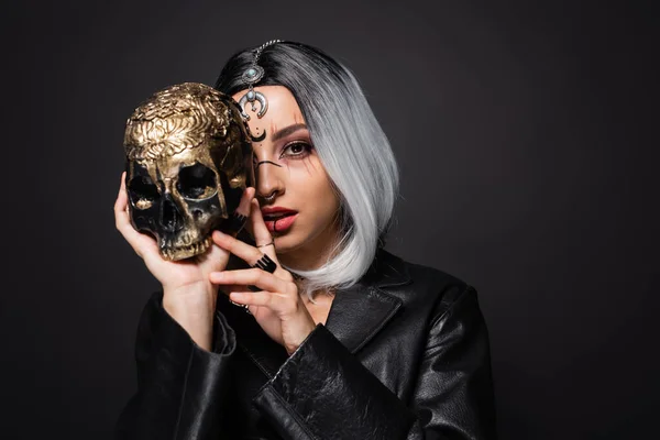 Young witch style woman with ash blonde hair obscuring face with spooky golden skull isolated on black — Stock Photo