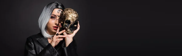 Frau in Hexenhalloween-Make-up mit beängstigendem goldenen Totenkopf in Gesichtsnähe isoliert auf schwarz, Banner — Stockfoto